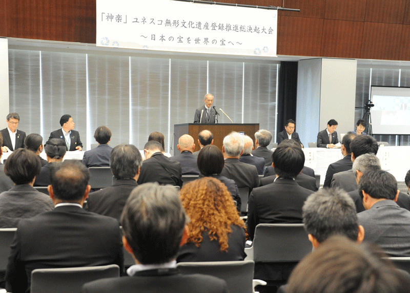 挨拶する後藤会長㊤、神楽の実演として高千穂の夜神楽から「戸取」を㊦
